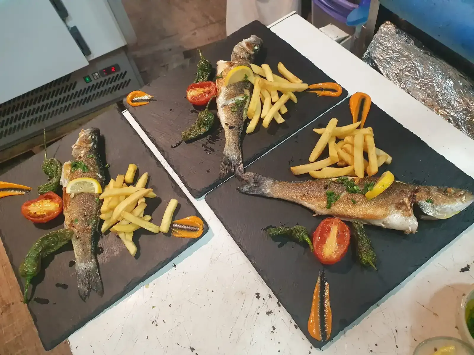 Tres platos de pescado con patatas fritas y guarnición de tomate, servidos en tablas negras.