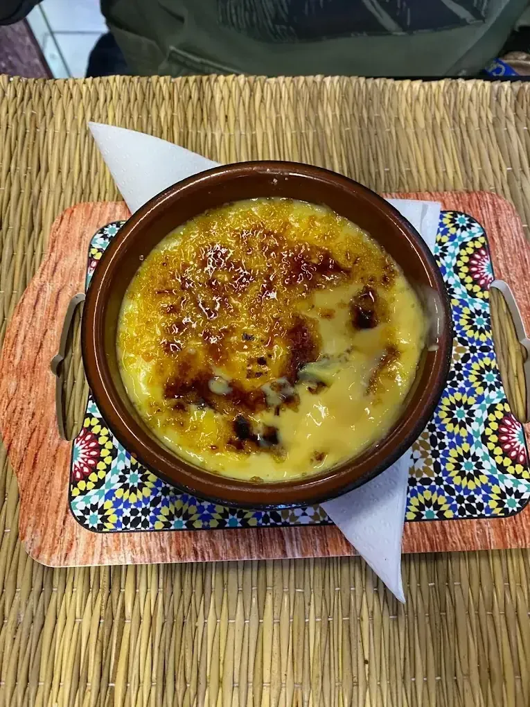 Postre horneado en un tazón marrón sobre un mantel individual colorido, con cobertura dorada sobre una mesa tejida.