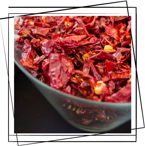 Un recipiente de vidrio lleno de pimientos rojos secos sobre una mesa.