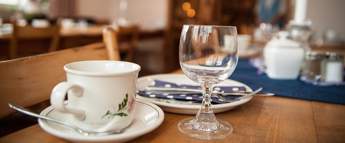 Kaffeetasse und Wasserglas auf einem Holztisch in einem Café, dazu eine blaue Serviette.