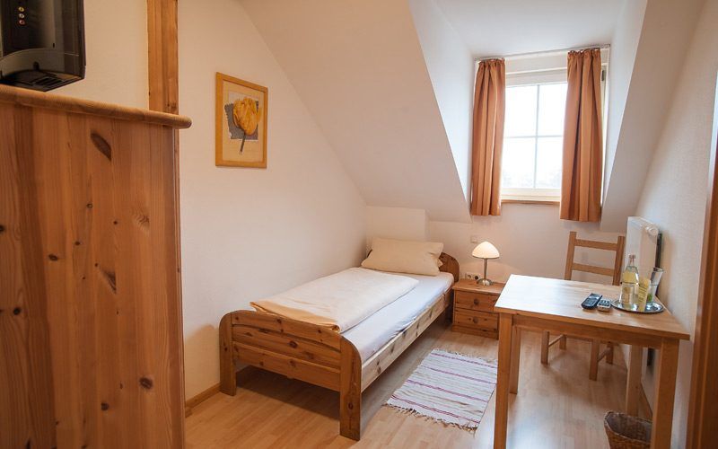 Kleines Dachzimmer mit Einzelbett, Holzschreibtisch und Fenster mit Vorhängen