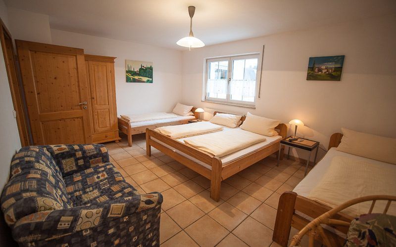 Helles Schlafzimmer mit zwei Holzbetten, gemustertem Sofa, Kleiderschrank, Fenster und Fliesenboden