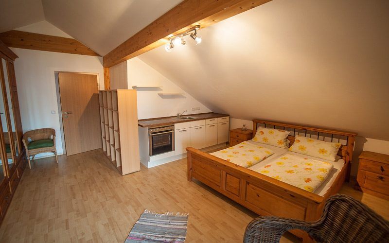 Gemütliches Dachgeschosszimmer mit zwei Einzelbetten, kleiner Küchenecke und schräger Holzdecke