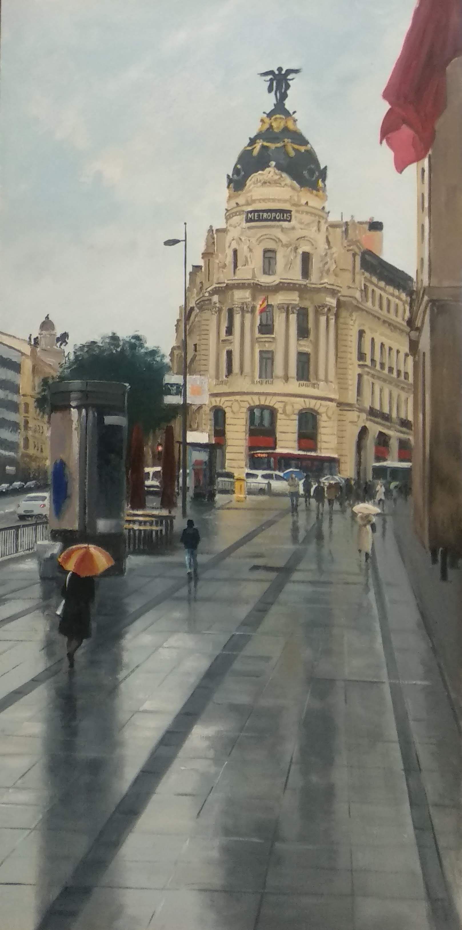 Un día lluvioso en Madrid con un edificio histórico y gente con paraguas caminando sobre el pavimento mojado.