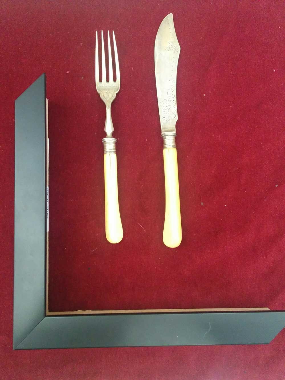 Tenedor y cuchillo con mangos amarillentos sobre fondo rojo, junto a un marco de imagen negro.
