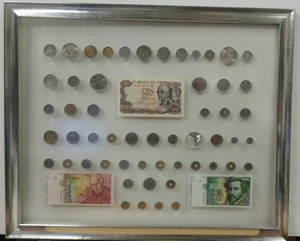 Colección enmarcada: diversas monedas y billetes expuestos sobre fondo blanco, en un marco plateado.