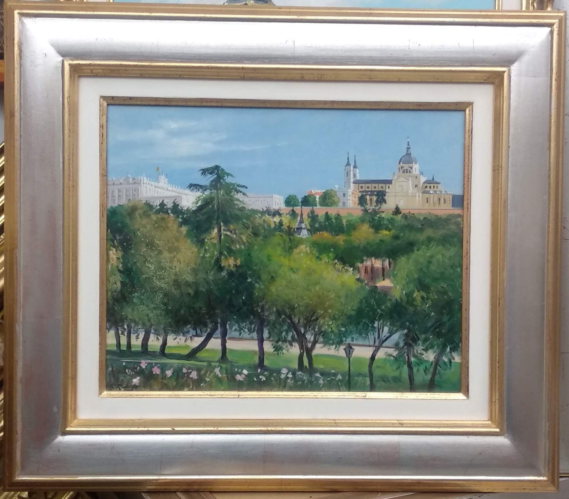 Cuadro de la Catedral de la Almudena de Madrid y el Palacio Real desde un parque, con árboles y cielo azul.