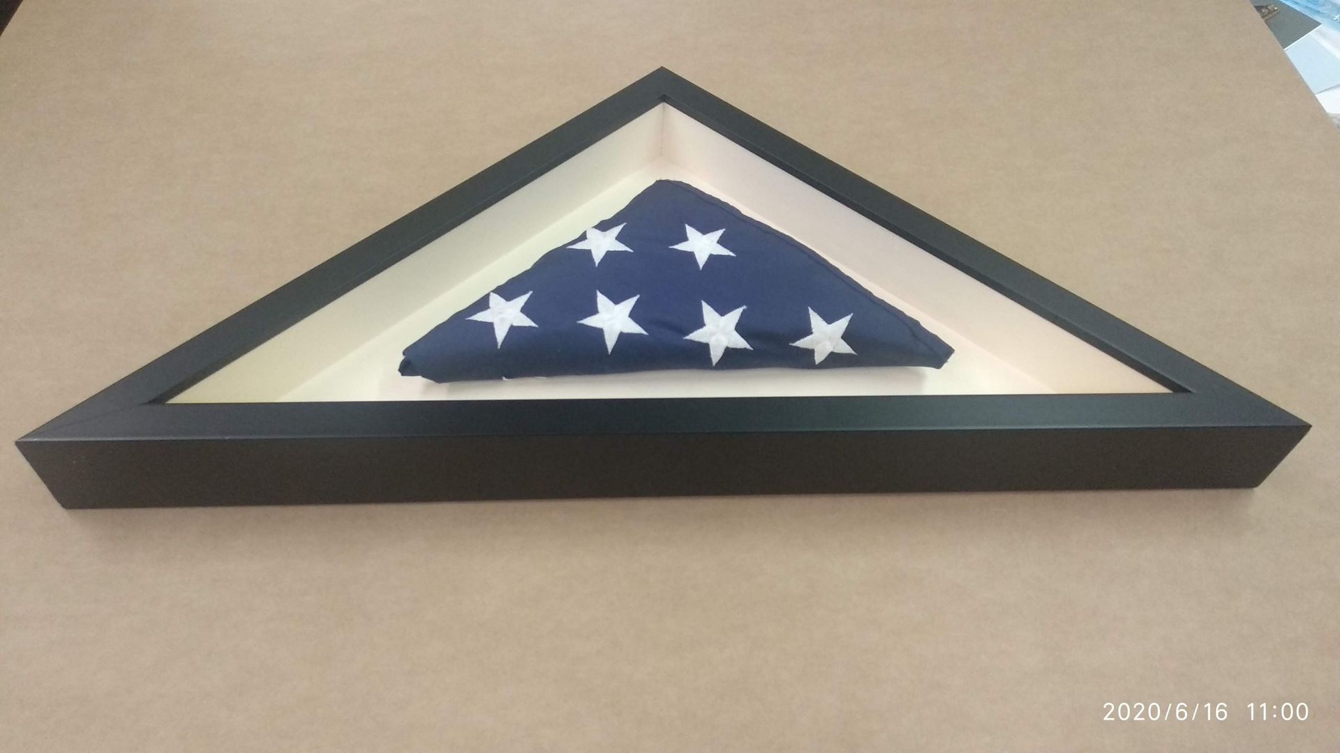 Bandera estadounidense doblada en una vitrina triangular negra sobre una superficie color canela.