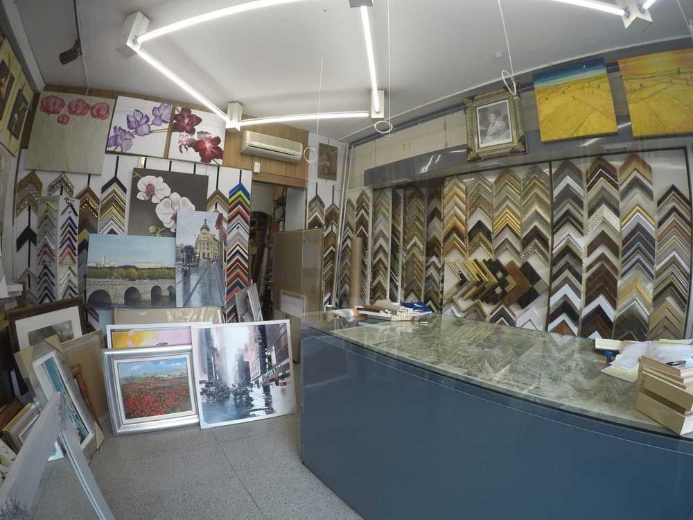 Dentro de una tienda de marcos, se exhiben diversos marcos y obras de arte, con un mostrador en primer plano.