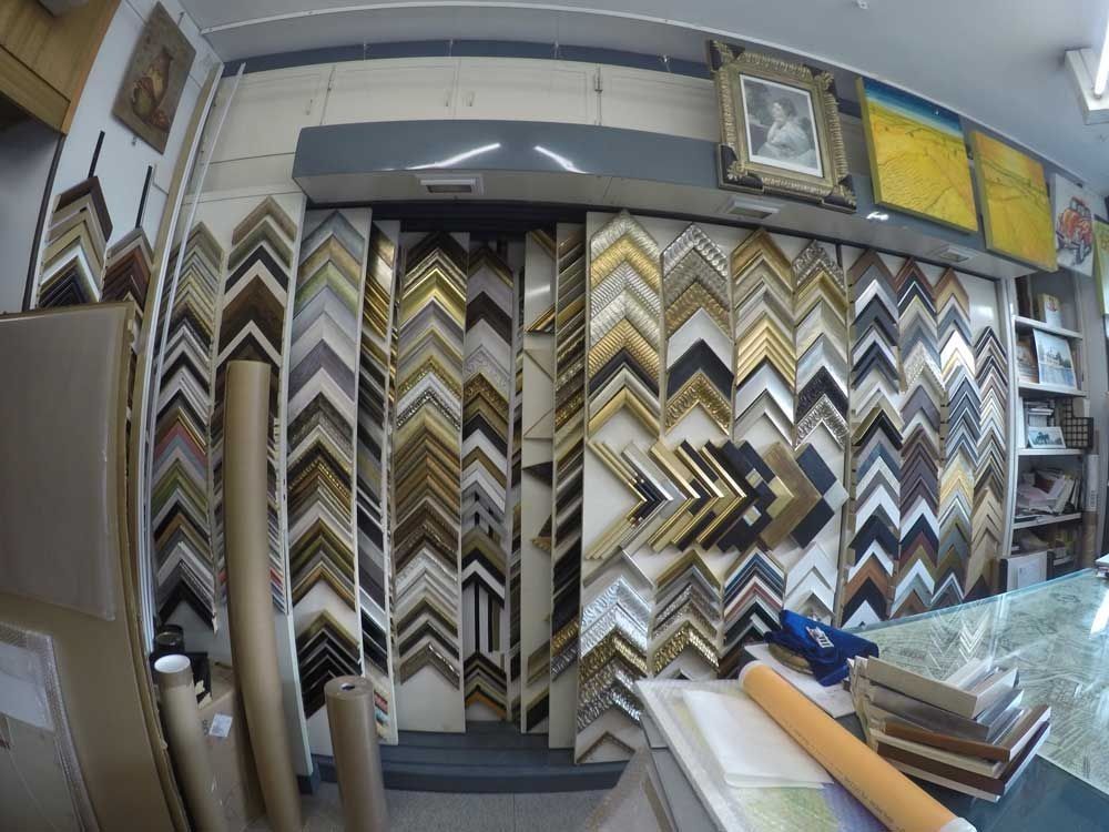 Dentro de una tienda de enmarcación, varias muestras de marcos de cuadros en tonos dorados, negros y madera.