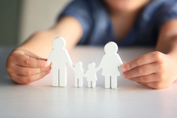 Enfant tenant des figurines en bois blanc représentant une famille de quatre personnes.