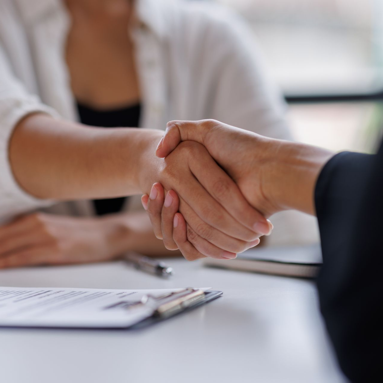 Deux personnes se serrent la main au-dessus d'un bloc-notes posé sur un bureau.