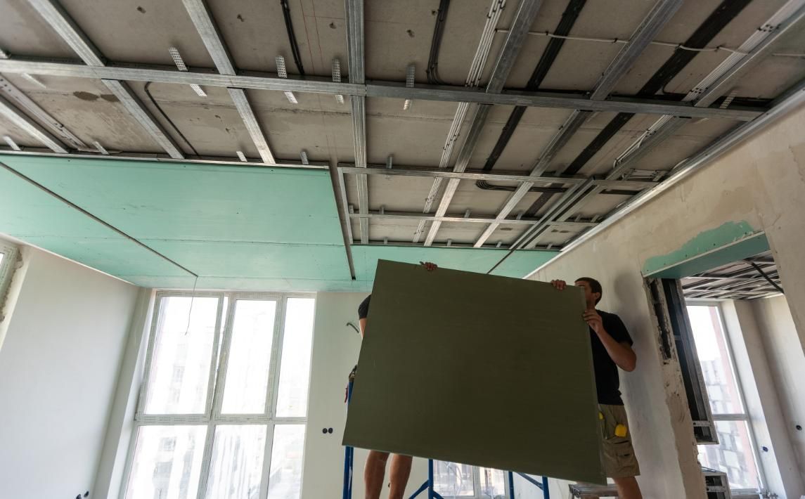Una persona sostiene un gran panel verde mientras trabaja en el techo de una habitación sin terminar.