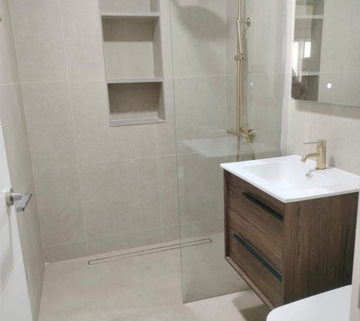 Baño moderno con ducha, paredes de azulejos blancos y tocador de madera con lavabo blanco.
