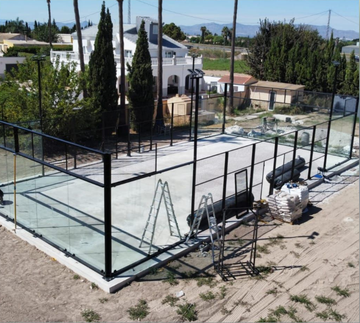 Pista deportiva exterior vallada en construcción, con base de hormigón blanco y estructura metálica negra