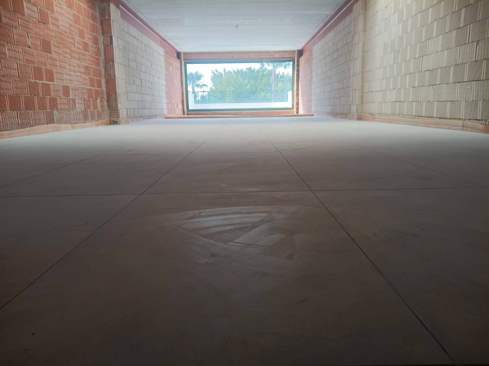 Pasillo interior vacío con suelo de baldosas que conduce a una luminosa abertura exterior con árboles