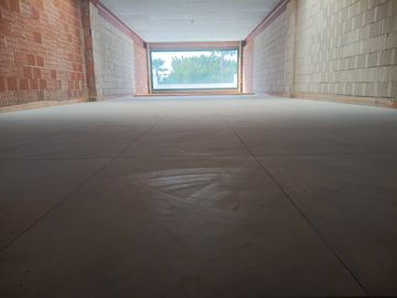Pasillo interior vacío con suelo de baldosas que conduce a una luminosa abertura exterior con árboles visibles