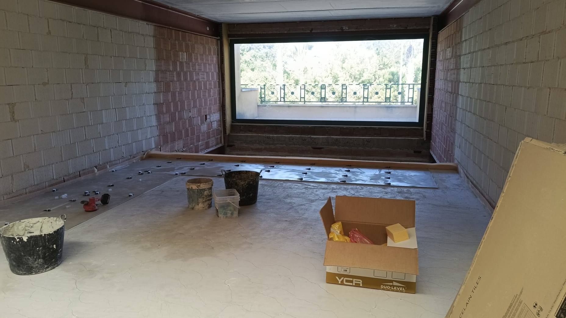 Habitación vacía con paredes blancas, suelo cubierto con una lona, ​​cubos de pintura y una gran ventana al fondo.