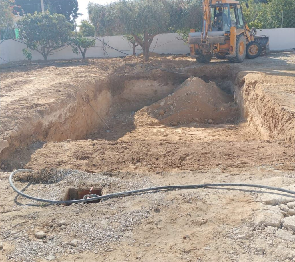Excavadora en una obra de excavación de tierra con una gran zanja y una manguera en el suelo.