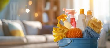 Seau bleu contenant des produits et des chiffons de nettoyage, posé sur une table dans un salon baigné de soleil