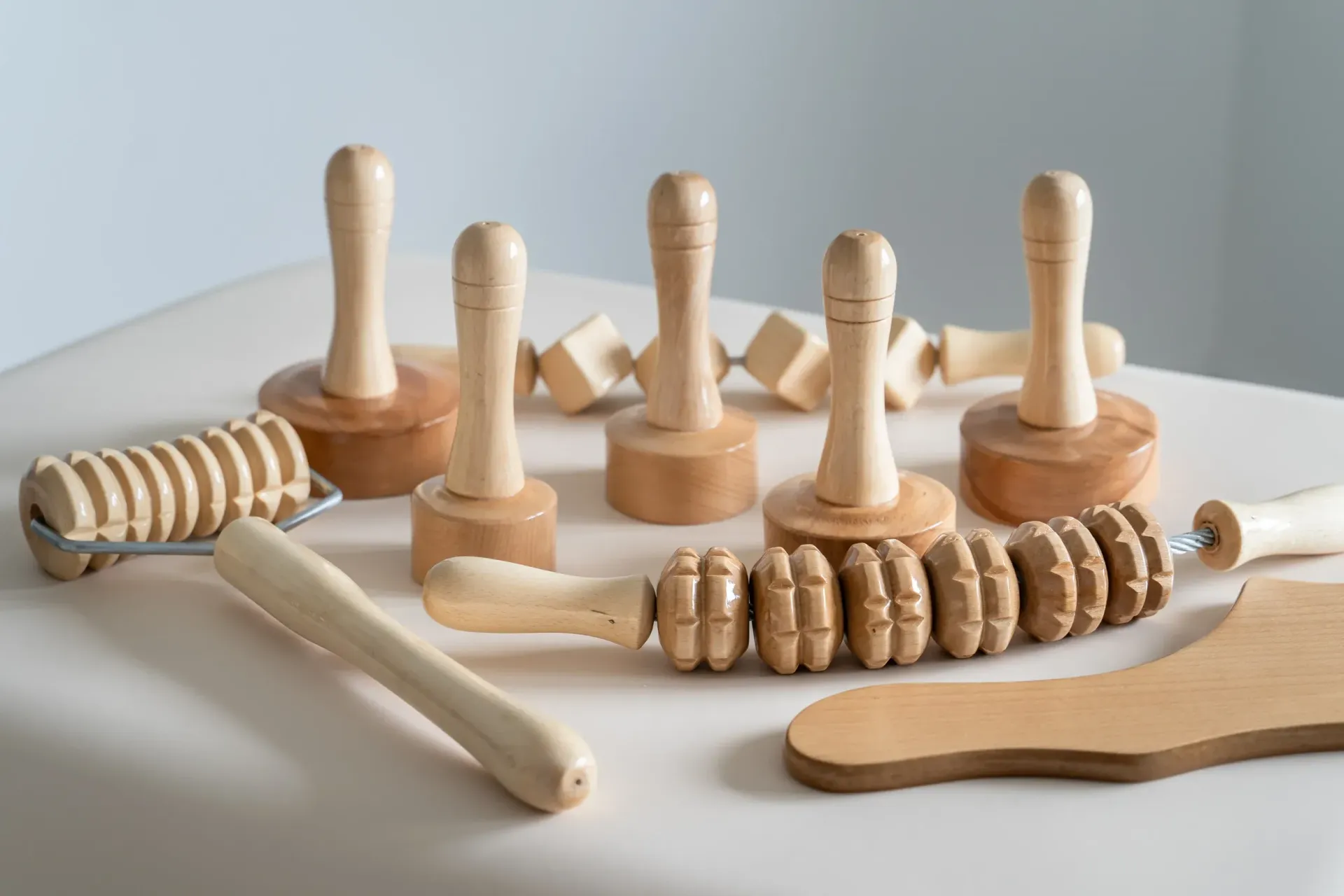 Herramientas de masaje de madera exhibidas sobre una superficie blanca, incluidos rodillos y masajeadores de mano.