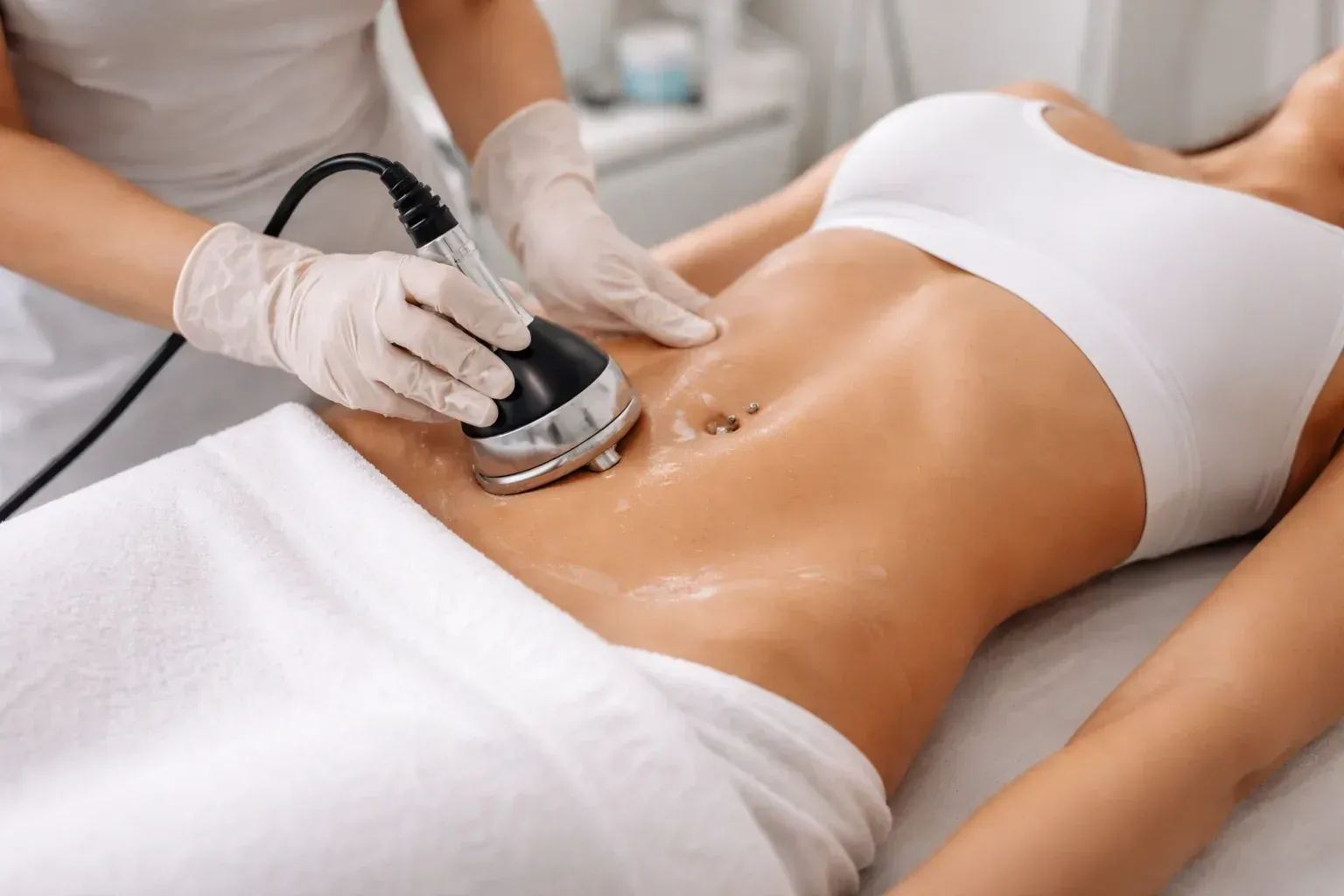 Persona recibiendo un tratamiento de contorno corporal en el abdomen. El técnico utiliza un dispositivo portátil en un spa.