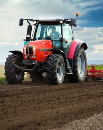 Un tractor rojo está arando un campo con un arado acoplado.