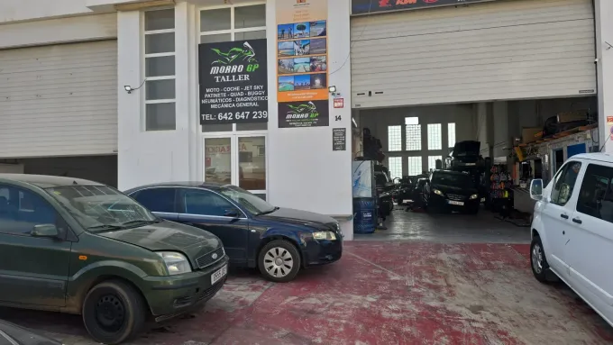 Coches aparcados fuera de un garaje con la puerta parcialmente abierta, mostrando equipamiento para motocicletas.