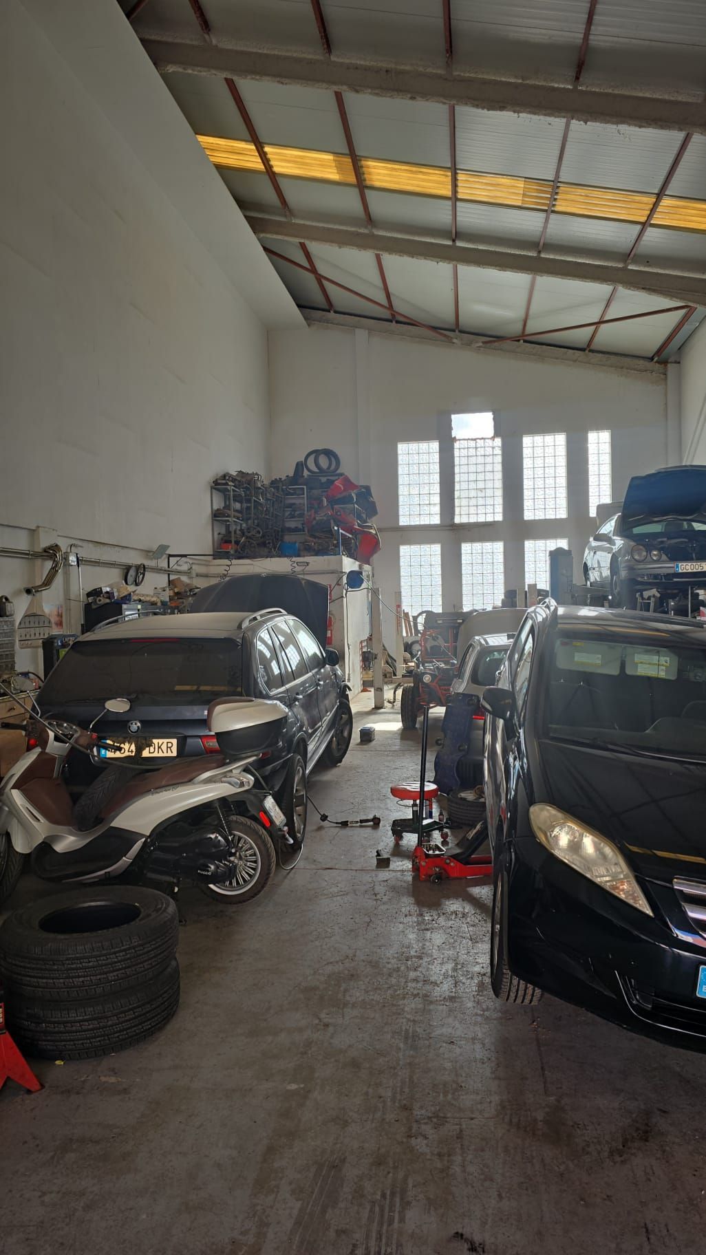 Autos dentro de un taller mecánico con equipo. Un auto en un elevador está junto a otros; las llantas están en el suelo.