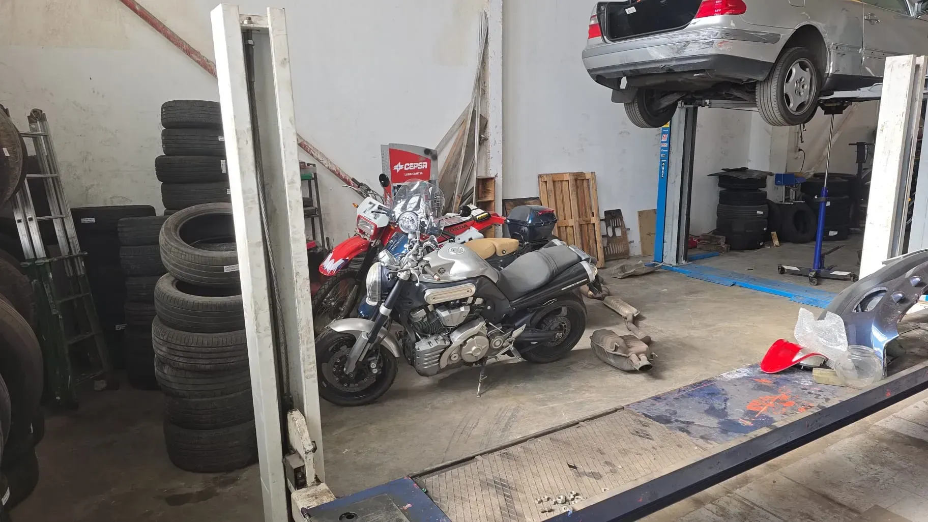Una motocicleta y un automóvil en un elevador en un garaje con neumáticos y equipamiento.