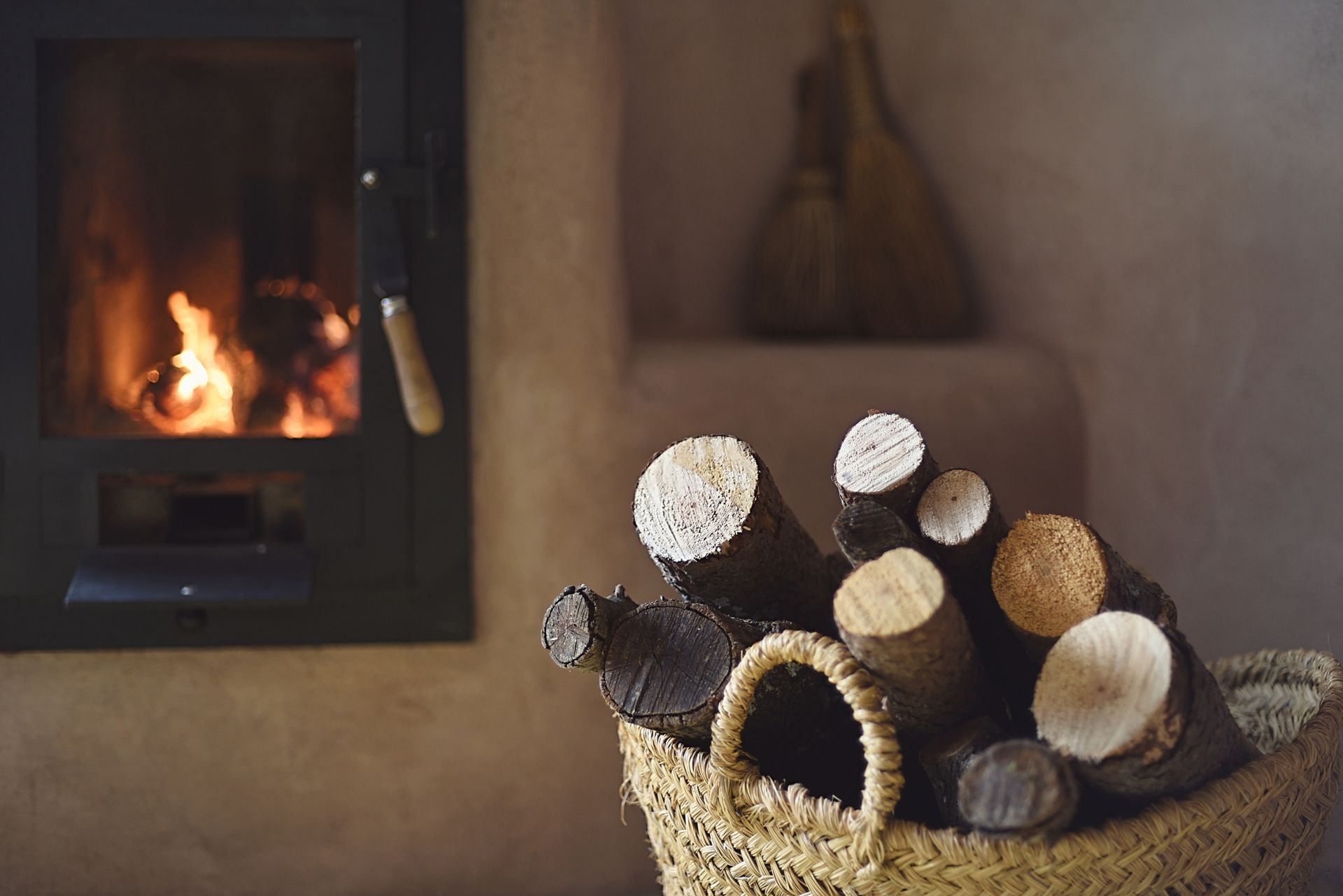 Uma cesta cheia de toras está em frente à lareira.