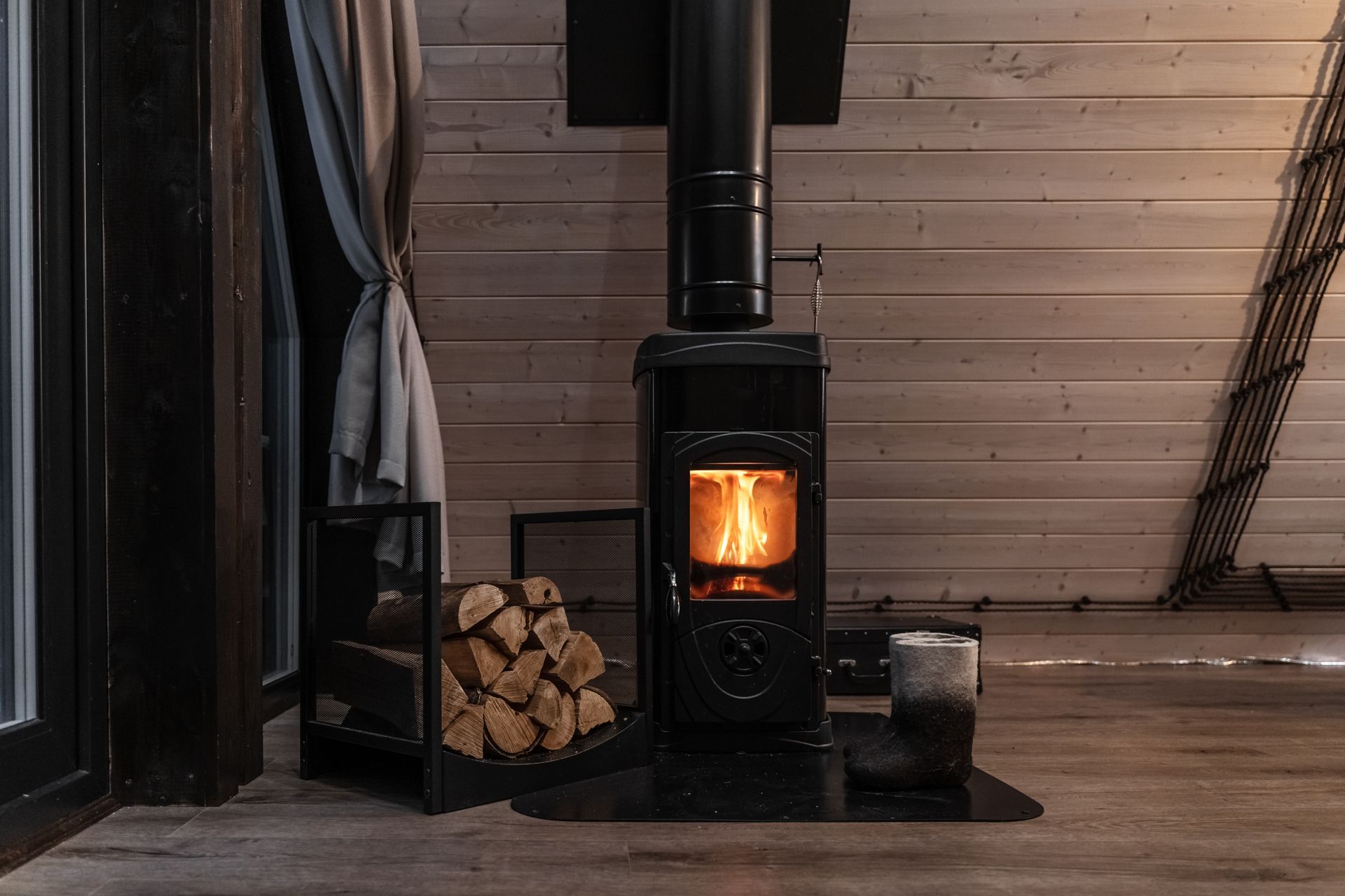 Um fogão a lenha está em uma sala ao lado de uma pilha de lenha.