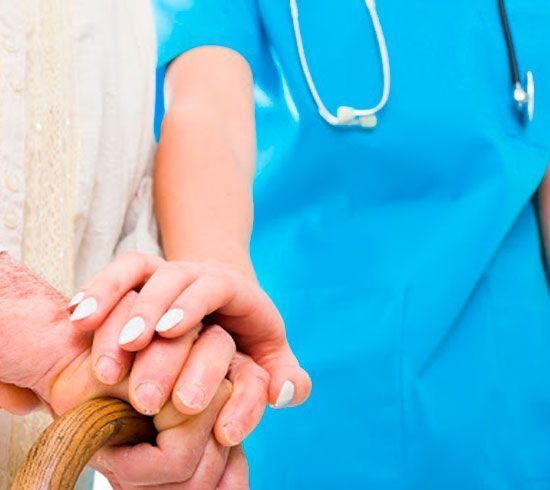 Una enfermera sostiene la mano de una anciana con un bastón.