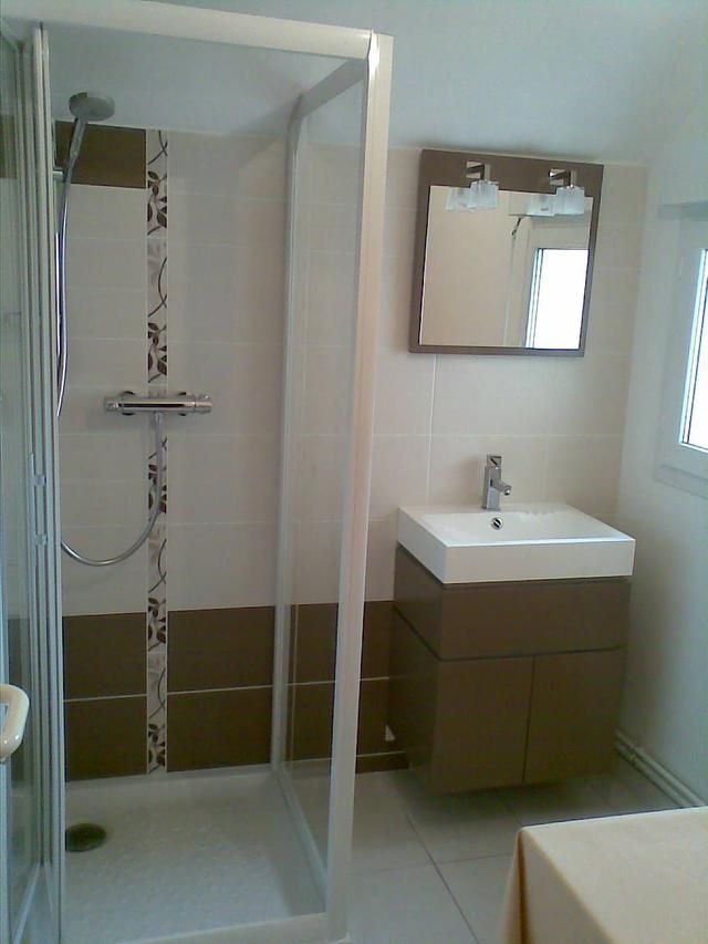 Salle de bains avec douche, meuble-lavabo et miroir ; murs carrelés de carrelage marron et blanc