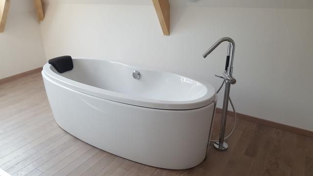 Baignoire ovale blanche avec robinetterie chromée dans une pièce aux tons clairs