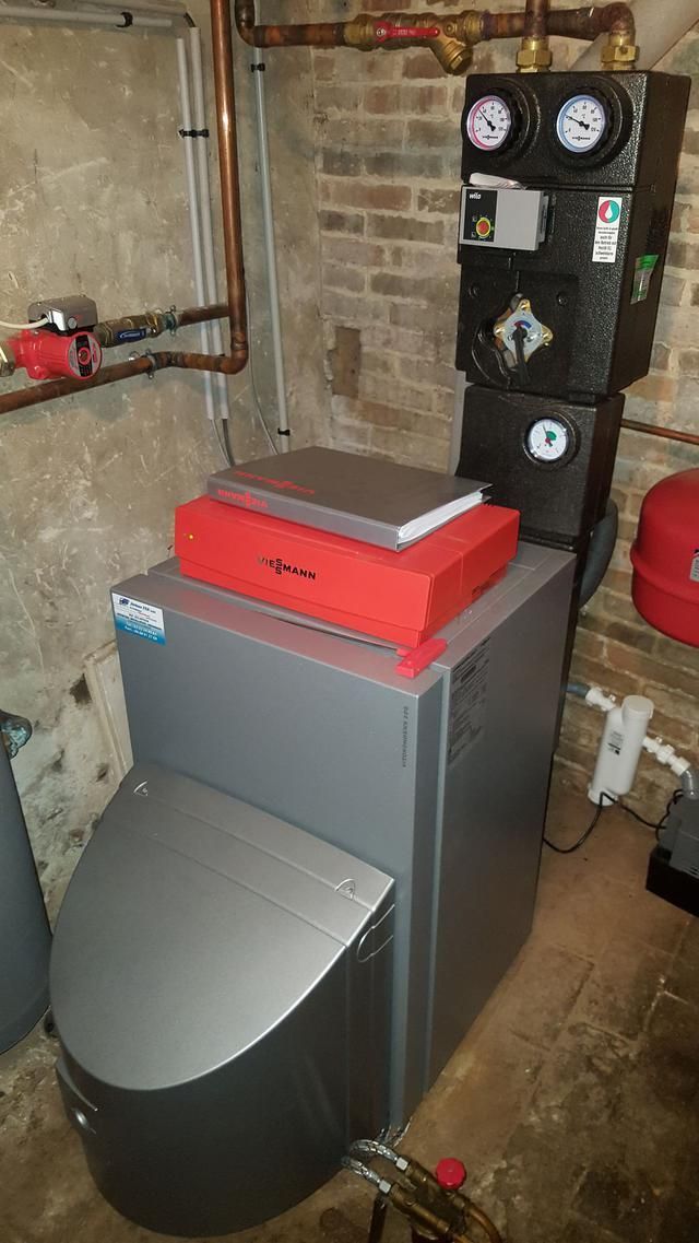 Un système de chaudière installé dans un sous-sol, avec des tuyaux en cuivre et un boîtier rouge au-dessus