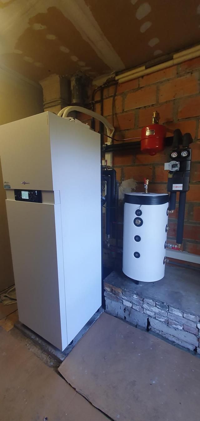 Un chauffe-eau et une chaudière blancs sont adossés à un mur de briques dans un sous-sol