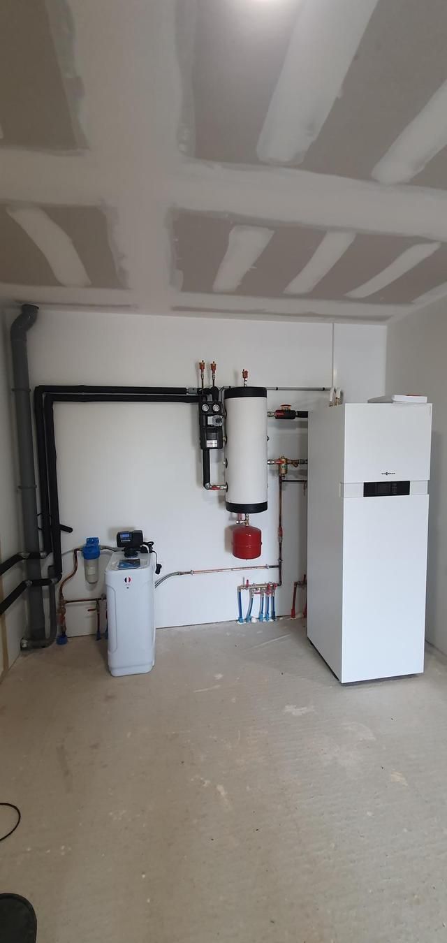 Local technique abritant un chauffe-eau et un système de distribution d'eau. Murs et plafond en placo, sol en béton.