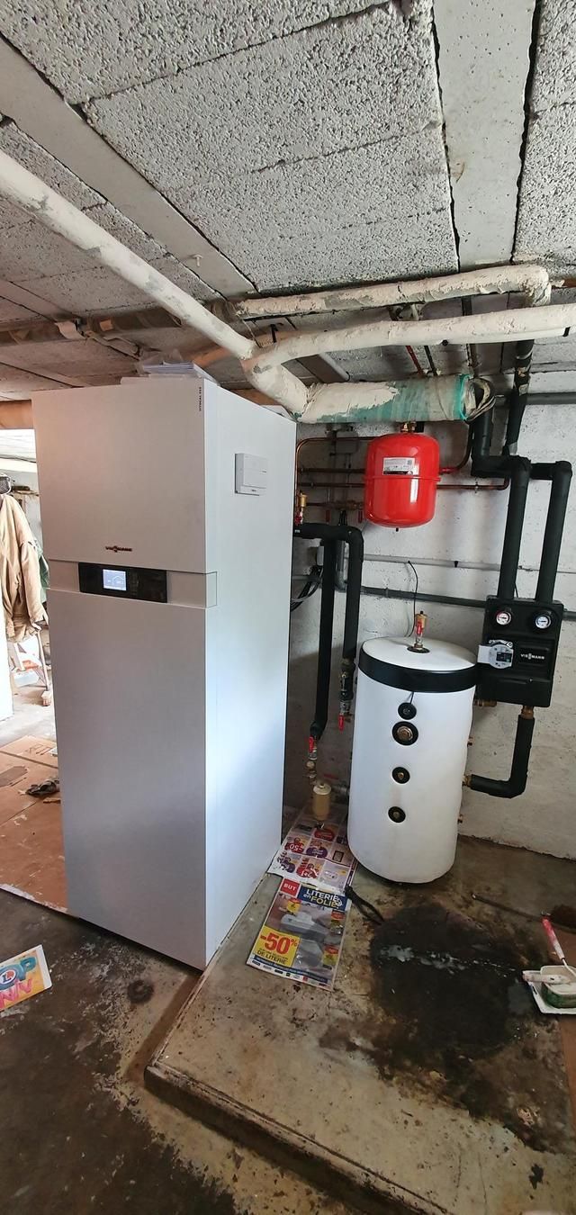 Un sous-sol avec un grand système de chauffage blanc, un réservoir rouge et un chauffe-eau sur un sol en béton