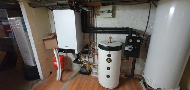 Une buanderie avec une chaudière blanche, un chauffe-eau et diverses canalisations