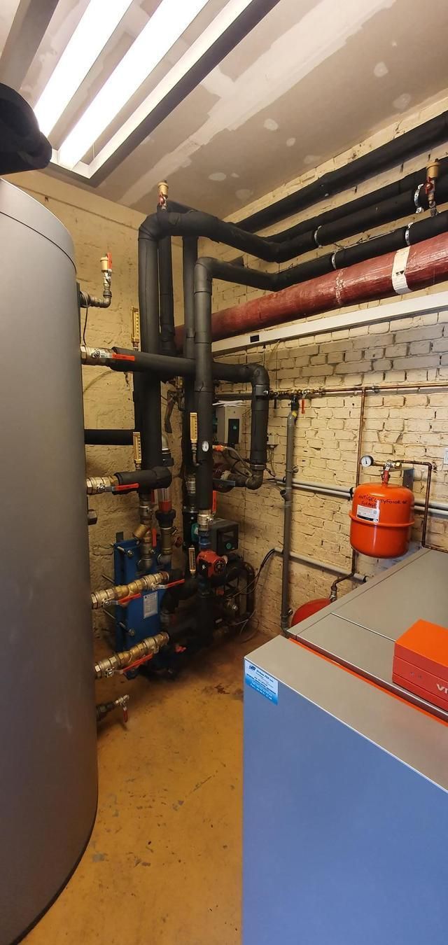 Une pièce contenant des tuyauteries et des équipements industriels, dont un chauffe-eau et une armoire bleue