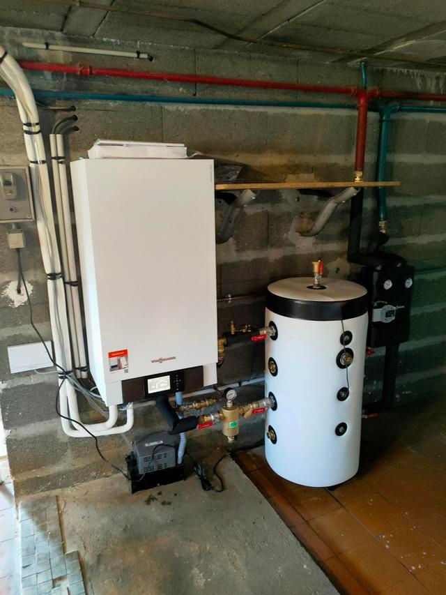 Chaudière blanche et ballon d'eau chaude avec tuyauterie en cuivre contre un mur en parpaings gris