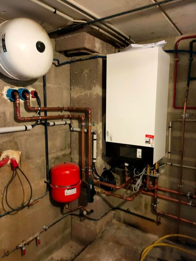 Système de chauffage dans un sous-sol avec une chaudière blanche, un vase d'expansion rouge et des tuyaux en cuivre