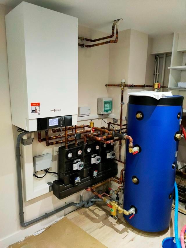 Chaudière blanche et réservoir d'eau bleu reliés par des tuyaux en cuivre et des composants noirs