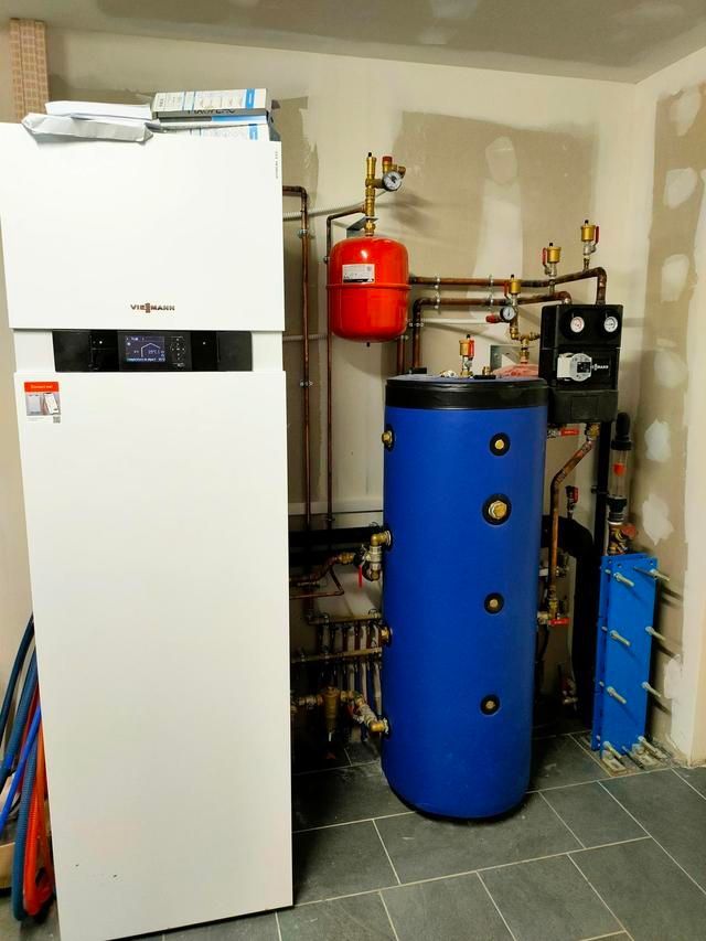 Appareil de chauffage blanc est placé à côté d'un réservoir d'eau bleu avec un vase d'expansion et des tuyaux en cuivre