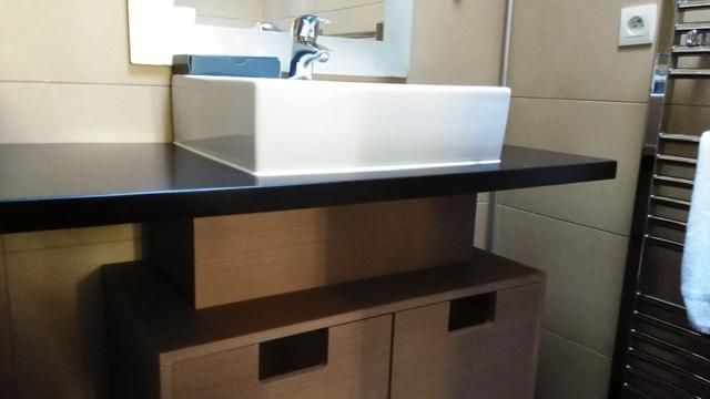 Lavabo rectangulaire blanc sur un plan de travail noir, au-dessus d'un meuble marron
