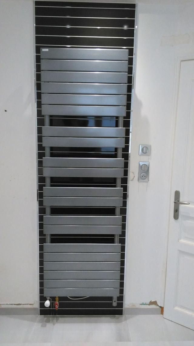 Radiateur argenté moderne fixé sur un mur avec carrelage noir