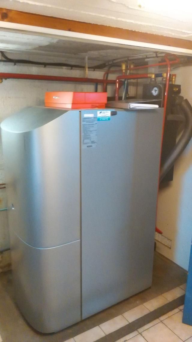 Grosse chaudière grise dans un sous-sol. Tuyaux rouges et noirs au plafond.