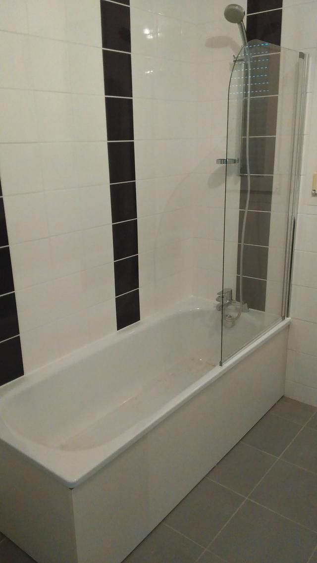 Baignoire blanche dans une salle de bains carrelée avec paroi de douche en verre et carreaux décoratifs foncés