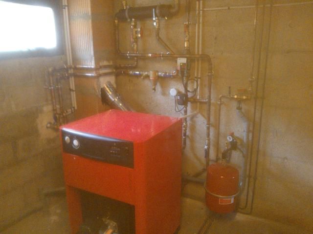 Unité de chauffage rouge avec tuyaux en cuivre et vase d'expansion dans un sous-sol